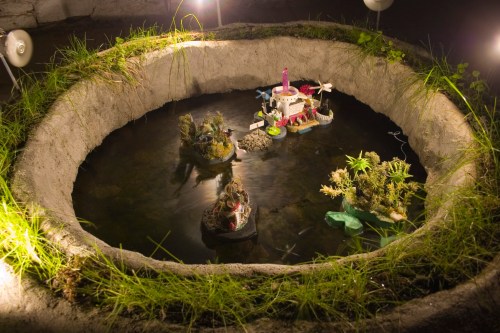 Earth pond.  A cement crater with miniature islands (Islands of Consumerism, Barren Wasteland, Extinction and Pristine Wilderness).  Live video feed of pond activity to Universe Room installation upstairs.